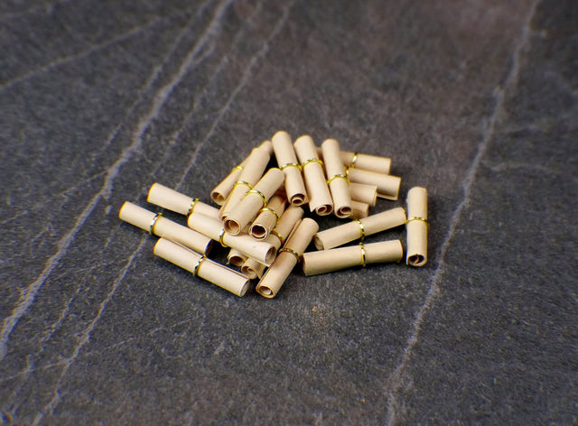 A pile of small, aged-looking parchment scrolls with metal rings on a textured dark background, likely representing blank spell paper for intentions and magical writings.