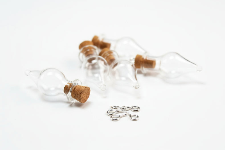 Glass bottles with cork stoppers and small metal hooks on a dark fabric background