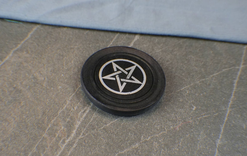 Black circular object with a white pentagram symbol on a stone surface