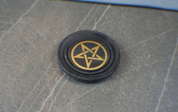 Black circular object with a gold pentagram symbol on a gray surface