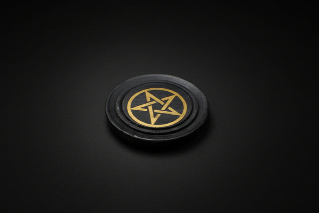 Black circular object with a gold pentagram symbol on a gray surface