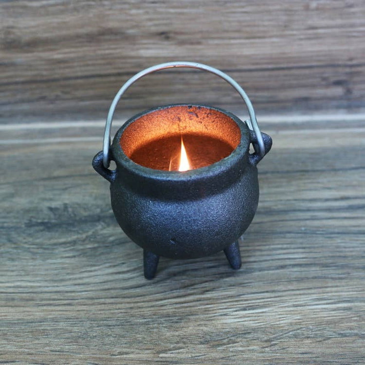 Small black cauldron-shaped candle holder with a lit candle on a wooden surface