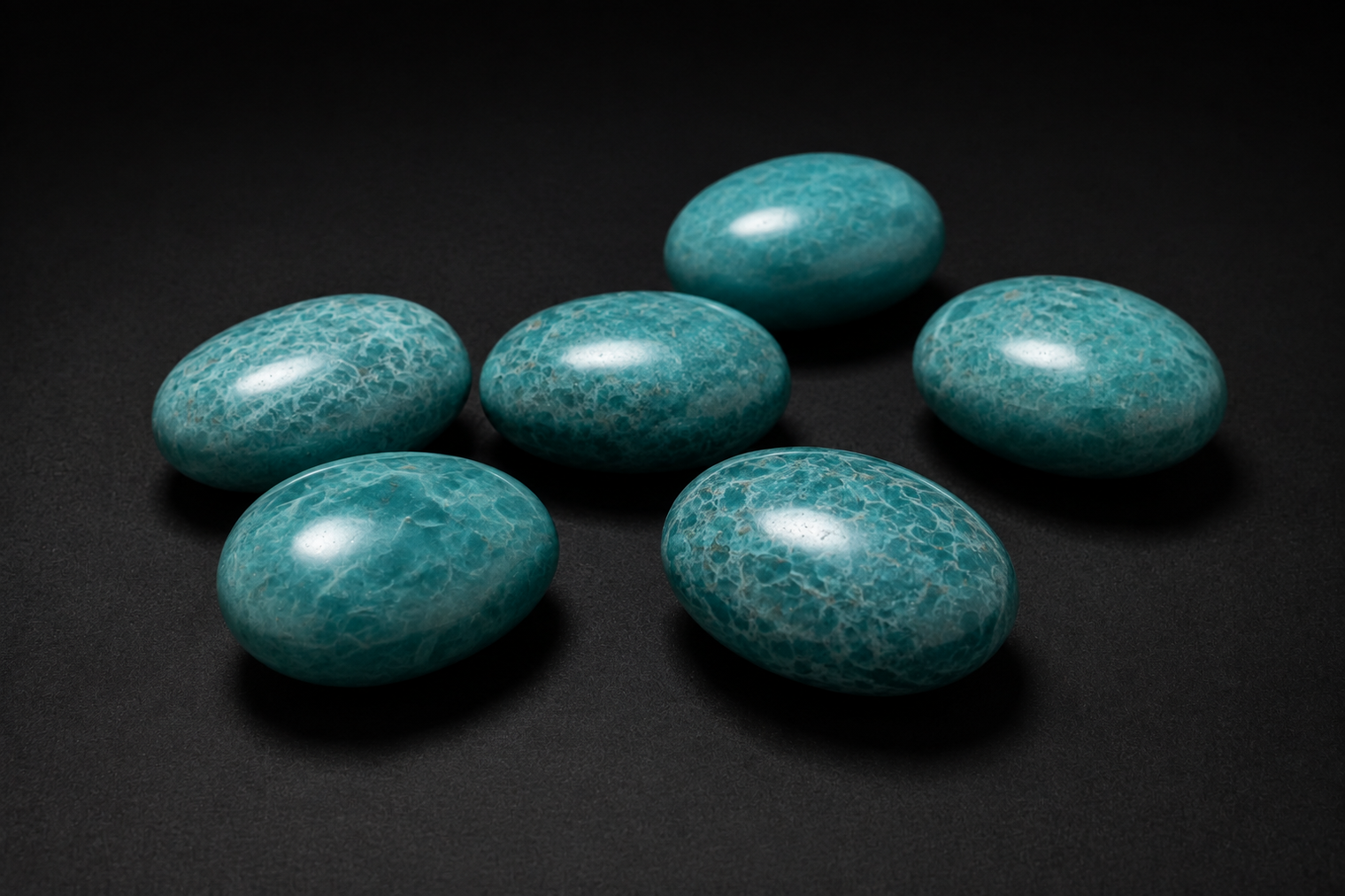 Six polished blue-green Amazonite palm stones with pale natural webbing on black