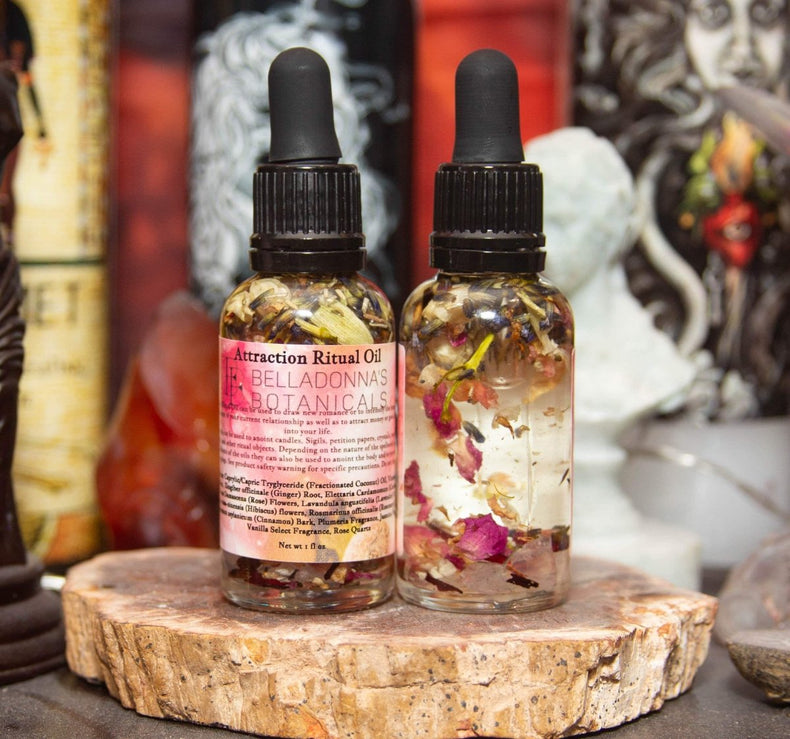 Two botanical oil bottles with attraction ritual oil and visible herbs on a wooden surface.