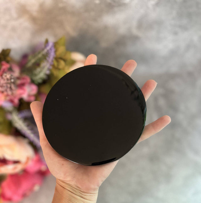 Hand holding a black round object with a blurred floral background