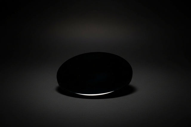 Hand holding a black round object with a blurred floral background