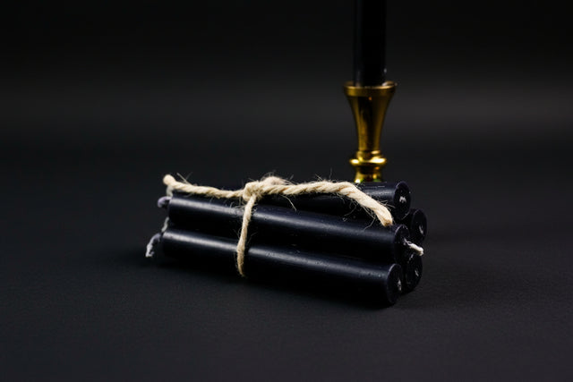 A small black chime candle tied with a string to a metal holder, set on a stone surface with a gold-colored handle.