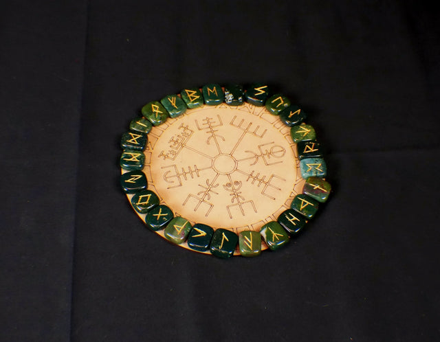A circular rune casting board with green and red patterns, and the Elder Futhark rune symbols carved into it.