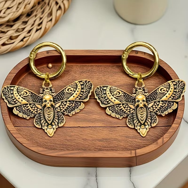 Pair of gold-tone death head moth boot charms showing skull-wing details and round clip rings