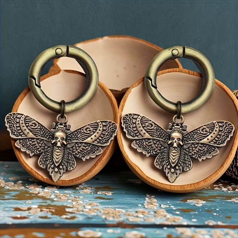 Pair of antique-brass-tone death head moth boot charms with skull motifs and round clip rings