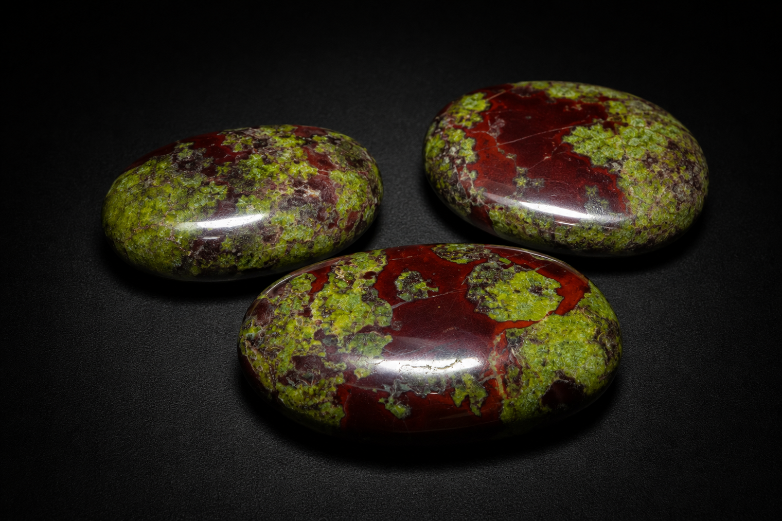 Three polished Dragon Blood Jasper palm stones with deep red and mossy green patterning on black