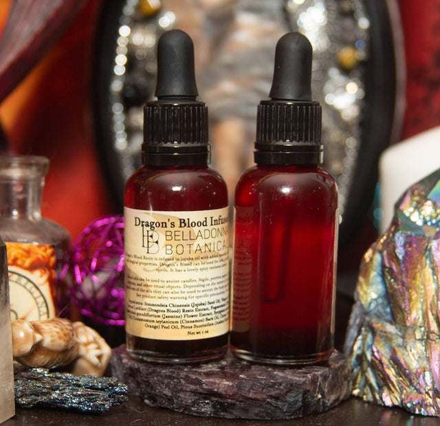 Two dropper bottles of dragons blood ritual oil, a red liquid on a dark surface with decorative items.