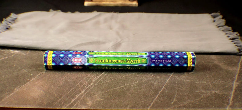 A pack of Frankincense & Myrrh incense sticks displayed horizontally on a wooden surface, with a colorful label visible.