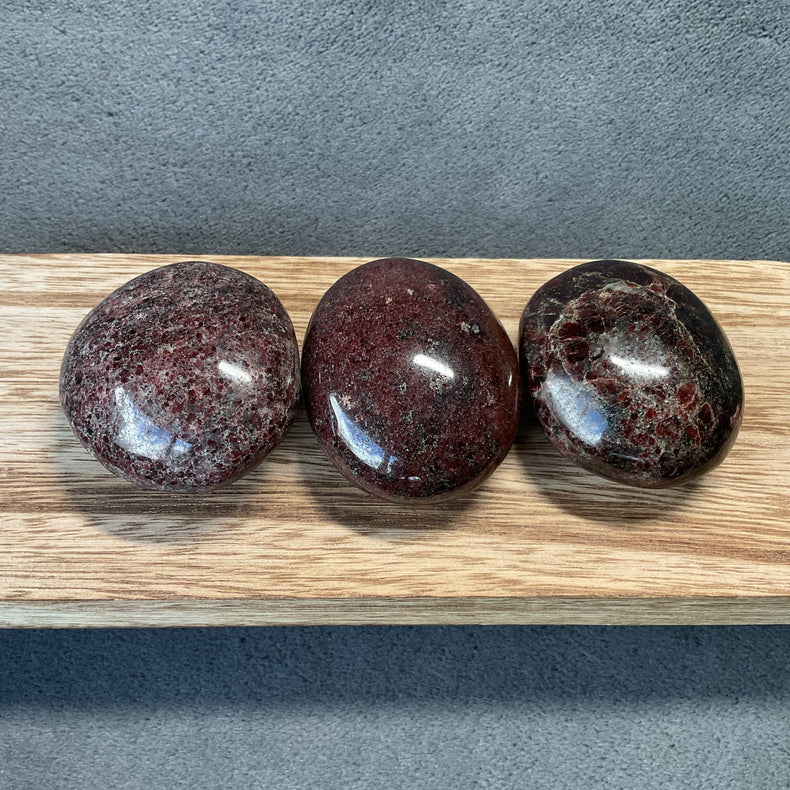 Three polished red stones on a wooden board with a gray background