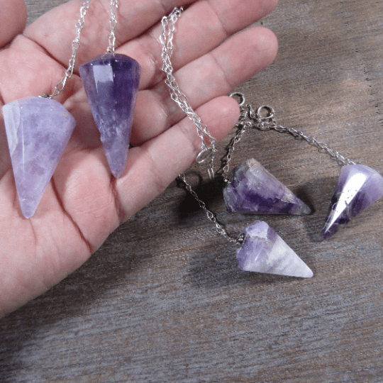 Hand holding a purple crystal necklace with another necklace on a wooden surface
