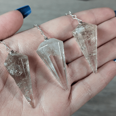 Three crystal pendants on silver chains held in a hand.