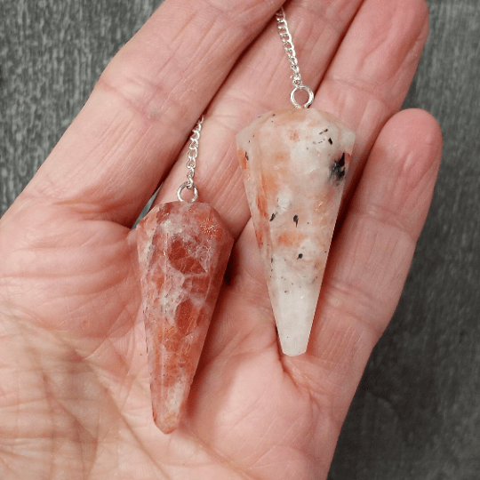 Two crystal pendants on silver chains held in a hand against a neutral background