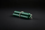Green chime candles tied with gold string, lit at one end, on a dark background with a copper bowl and herbs.