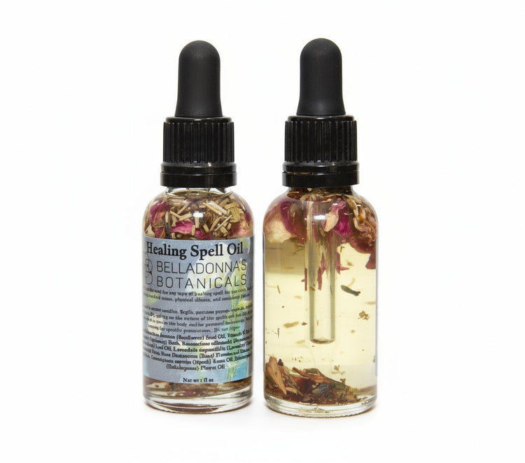 Two bottles of 'Healing Spell Oil' with botanicals on a dark surface.