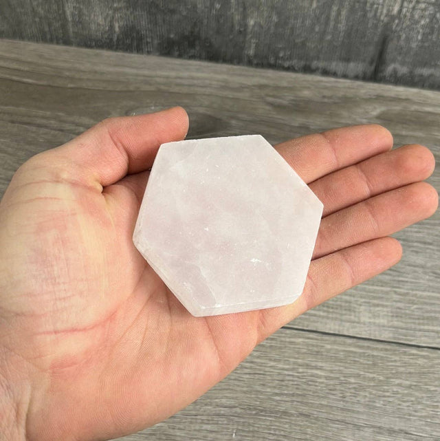 Hexagonal crystal held in a hand on a wooden surface