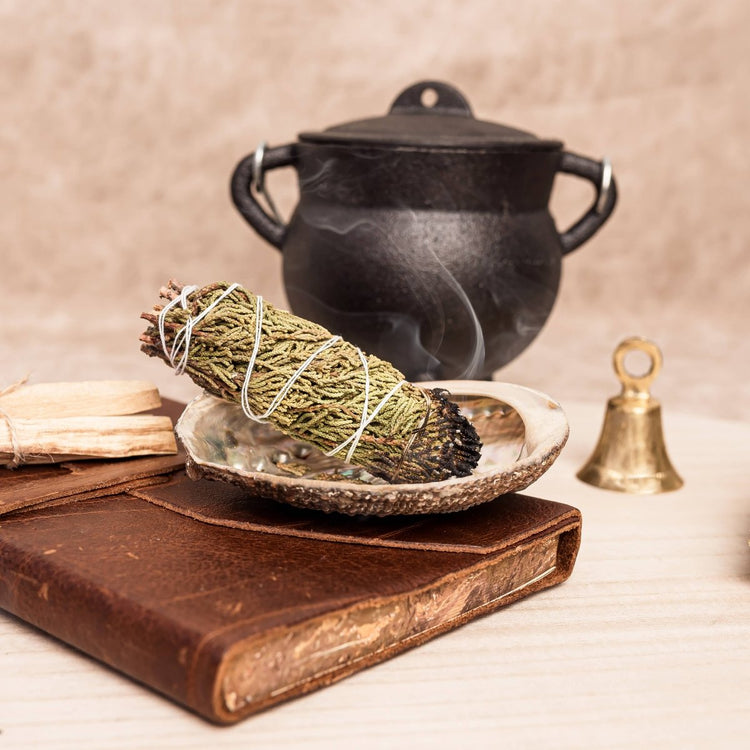 Sage bundle on a ceramic plate with a black pot and bell in the background