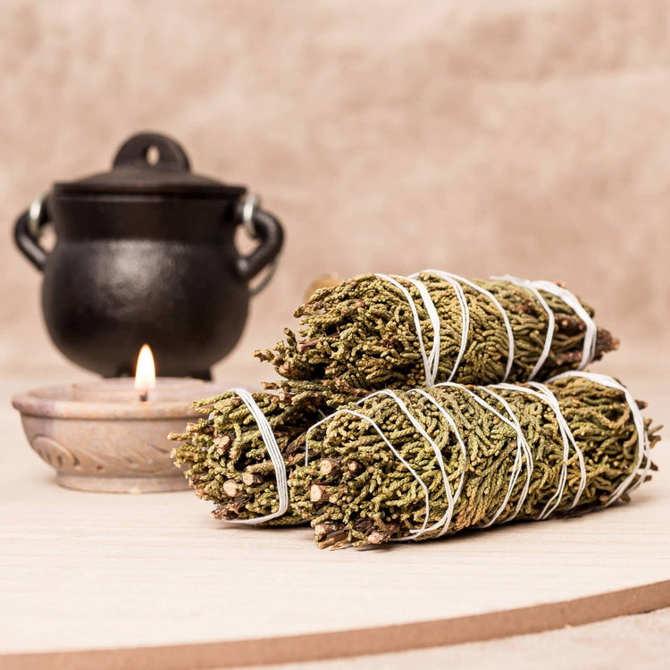 Two bundles of sage tied with twine on a wooden surface with a candle and black pot in the background.