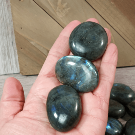 Hand holding three polished labradorite stones with a wooden background