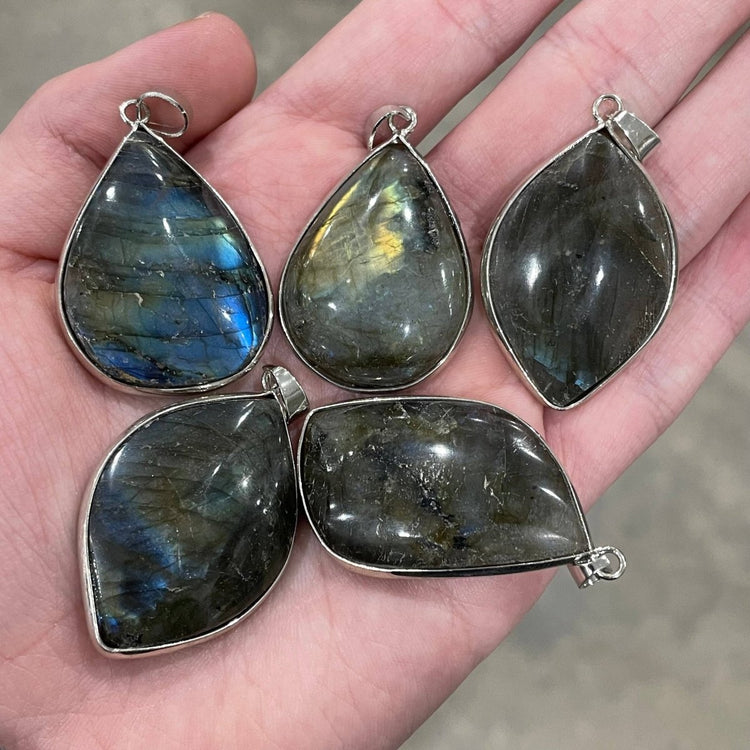 Five teardrop-shaped labradorite pendants with silver settings on a hand.