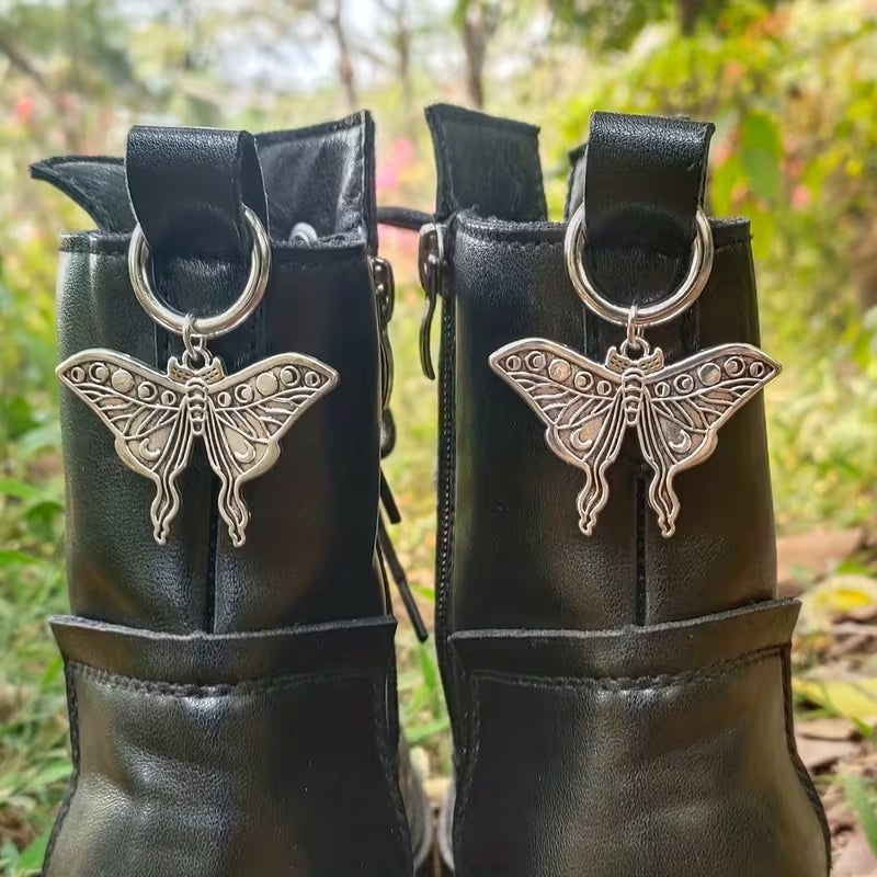 Pair of silver-tone lunar moth boot charms clipped to black boots outdoors