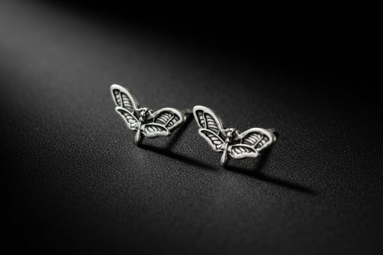 Black earring with butterfly design on a mannequin ear against a blurred background