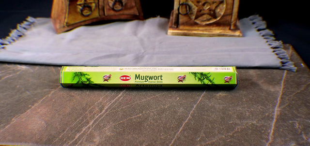 A box of Mugwort incense sticks placed on a table with a decorative item in the background.