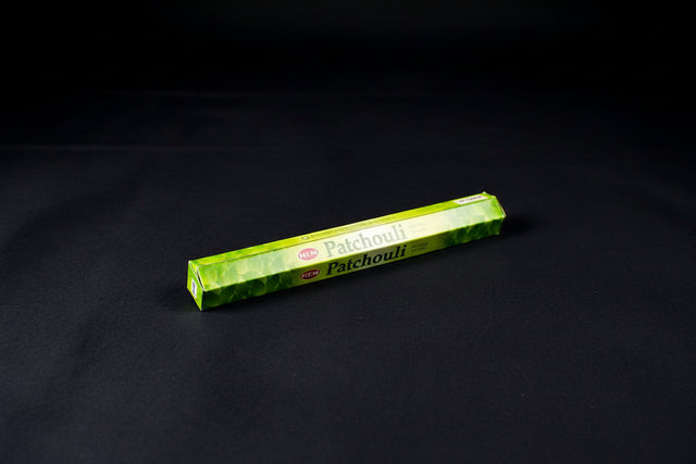 A pack of Patchouli incense sticks placed on a cloth beside a wooden box, with the name 'Patchouli' visible on the packaging.