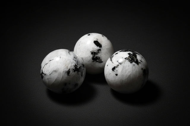 Hand holding a white marble-like sphere with black spots, surrounded by similar spheres on a wooden surface.