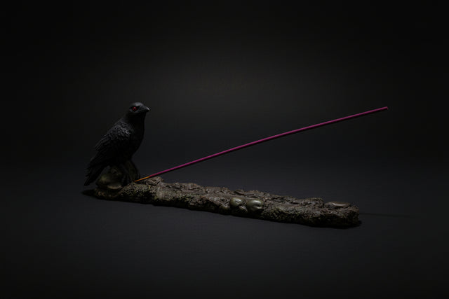 Incense burner with two black bird figurines and a purple incense stick on a white background