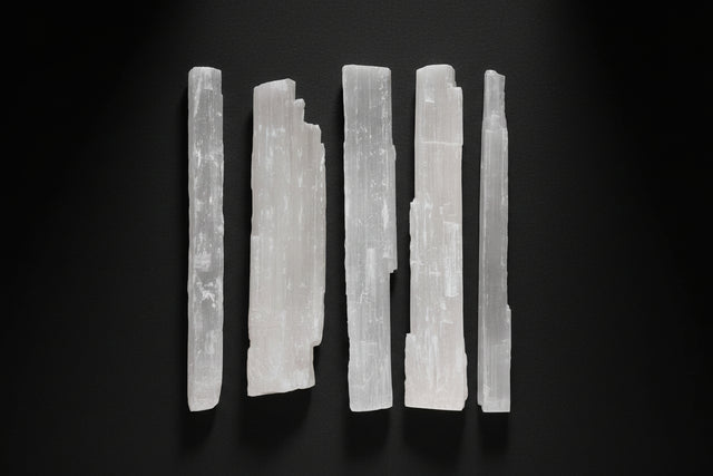 Set of six white selenite sticks on a white background