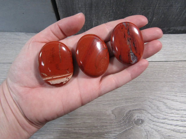 Three red jasper stones held in a hand on a wooden surface