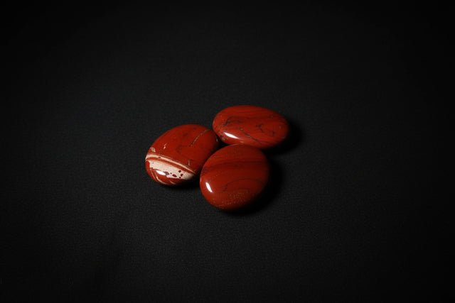Three red jasper stones held in a hand on a wooden surface