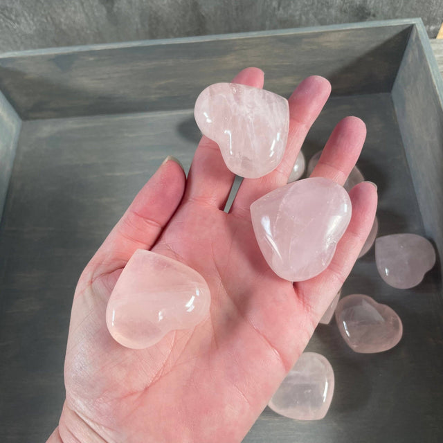 Heart-shaped pink crystals held in a hand with more crystals in the background.