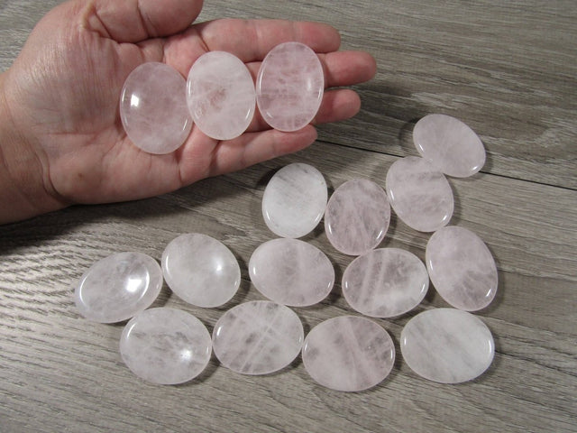Hand holding a rose quartz stone with more stones on a wooden surface