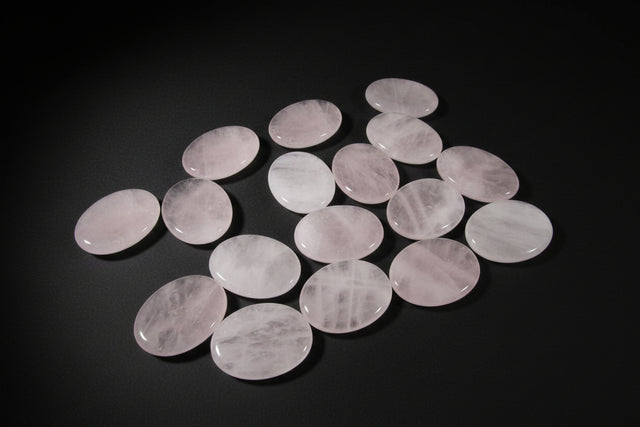 Hand holding a rose quartz stone with more stones on a wooden surface