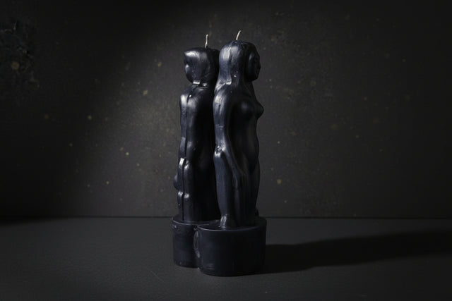 Black candle holders shaped like abstract human figures on a dark background with
