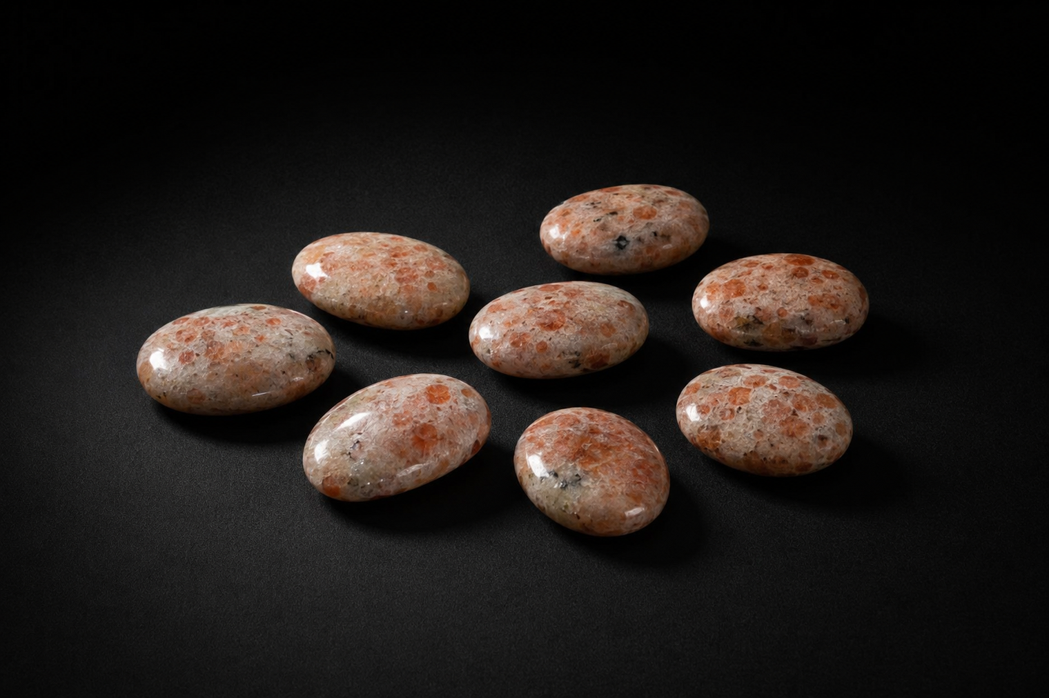 Eight polished peach and cream Sunstone palm stones with varied feldspar mottling on black