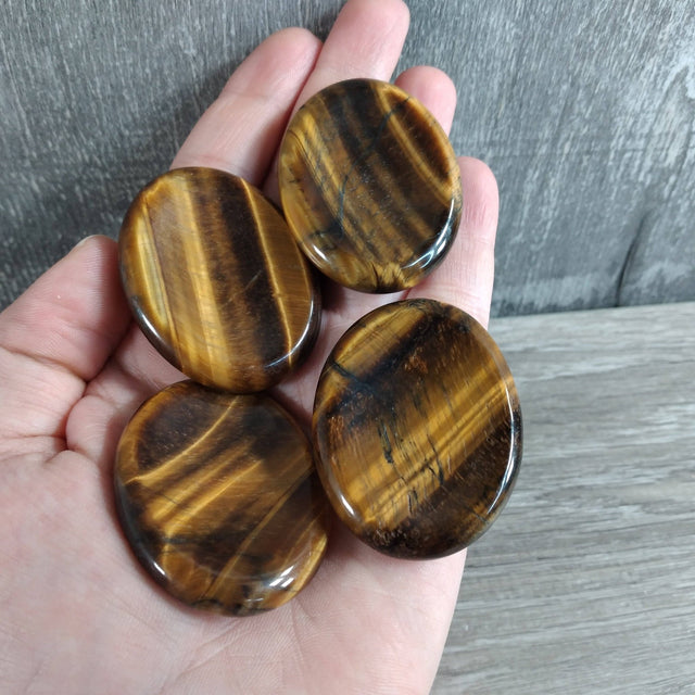 Four tiger eye stones held in a hand with a wooden surface in the background