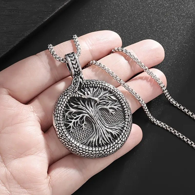 Silver tree of life pendant on a chain held in a hand against a dark background