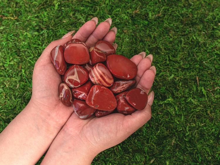 Hand holding red marbled jasper stones against a green grass background