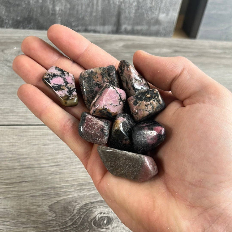 Hand holding a collection of rhodonite crystals on a wooden surface