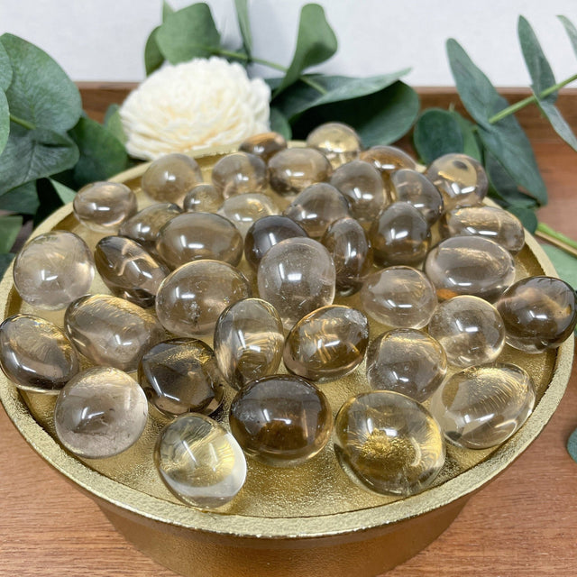 Clear glass stones on a gold tray with greenery and a white flower in the background