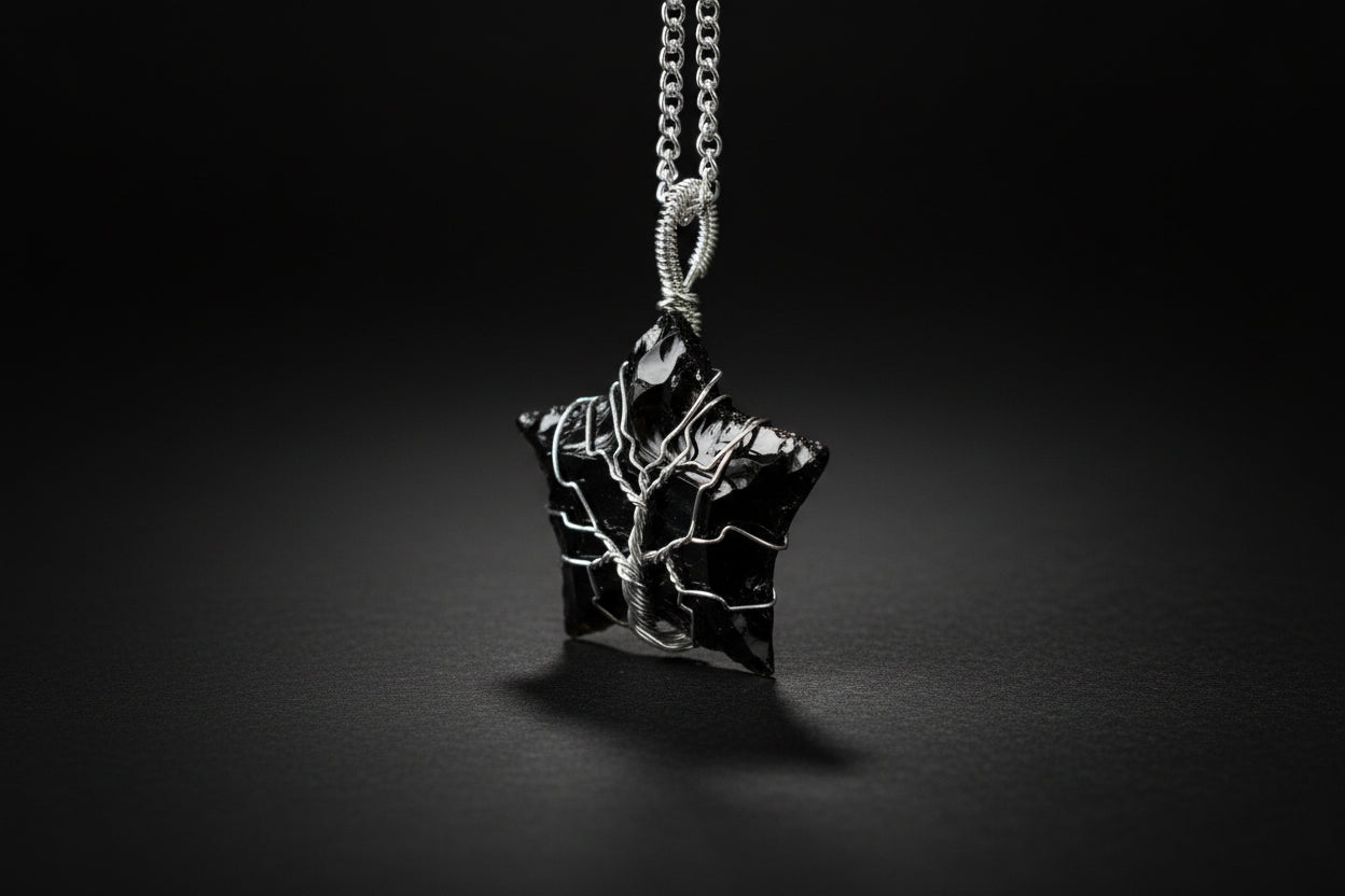 Black obsidian star-shaped pendant on a chain against a green blurred background