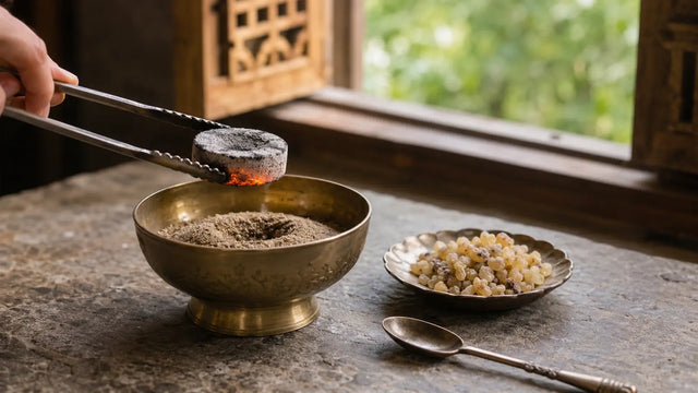 Glowing charcoal disc held with metal tongs above a sand-filled brass bowl beside frankincense resin