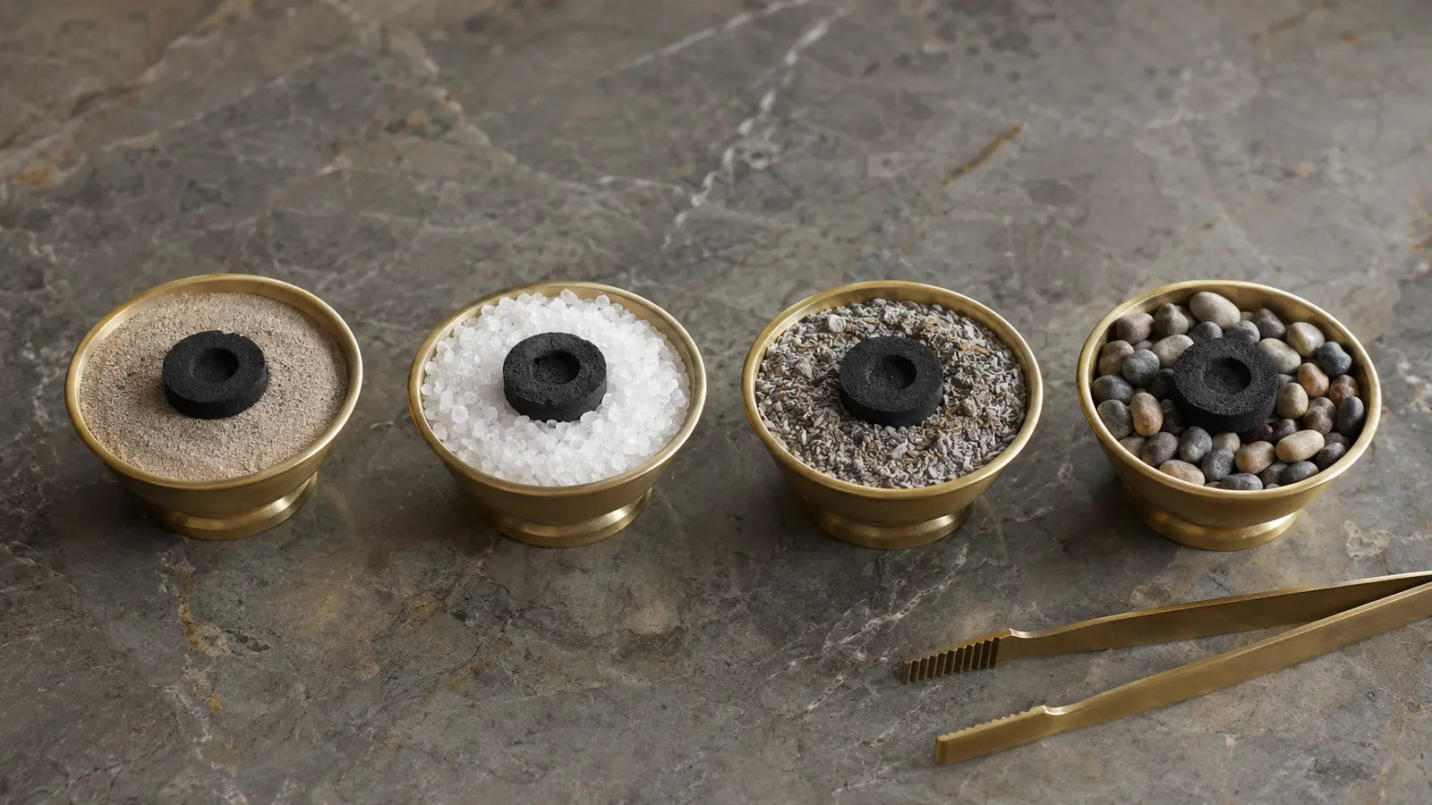Four brass bowls filled with sand, salt, ash, and pebbles beneath unlit incense charcoal discs